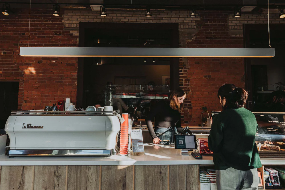 Dark Horse Espresso | Guest and barista at counter with red brick wall in the background | Homes Almanac