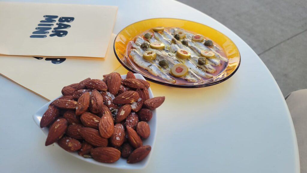 Afternoon in Leslieville | Olives & anchovies on an orange plate and a triangle shaped bowl of almonds sitting on a white table next to 2 menus of Bar Mini | Homes Almanac