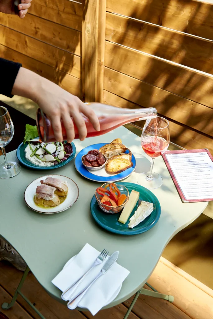 Ossington Wine Crawl | A hand pouring a glass of rose wine with different snacks on plates sitting on a green table | Homes Almanac