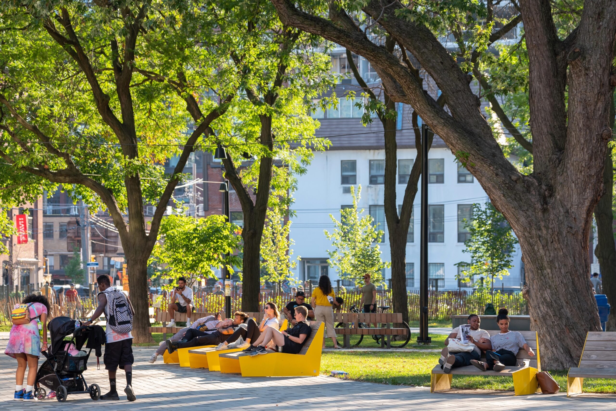 Historic Downtown Toronto Park | A sunny day in St. Andrew's Playground Park with mature trees and people sitting on yellow seating | Homes Almanac