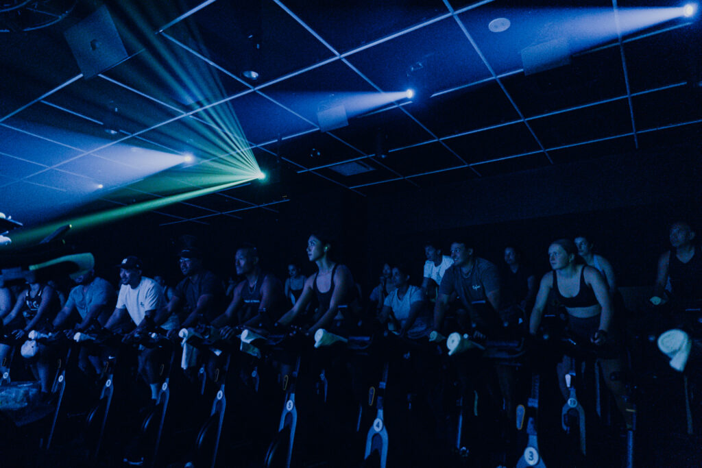 King and Portland | A darkly lit spin class inside Sweat & Tonic with participants on spin bikes | Home Almanac