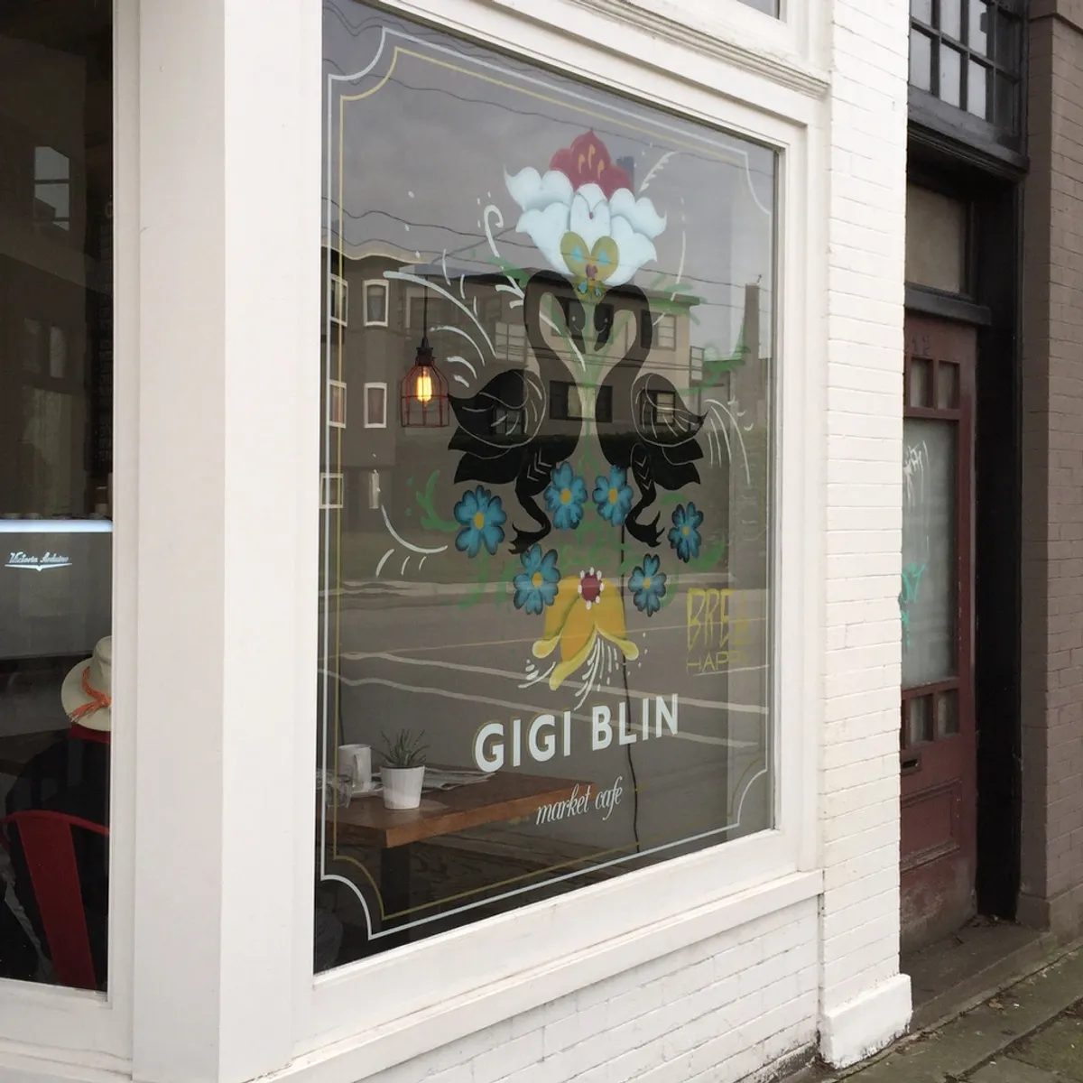 Gigi Blin Market Cafe Vancouver | White brick exterior facade with Gigi Blin logo on window and painted black swans | Homes Almanac