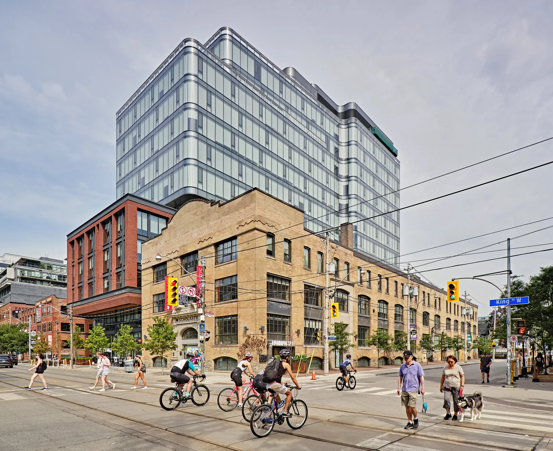 King and Portland | The corner of King St W and Portland St with brick facade buildings, glass tower behind and bikers and pedestrians crossing the street | Homes Almanac