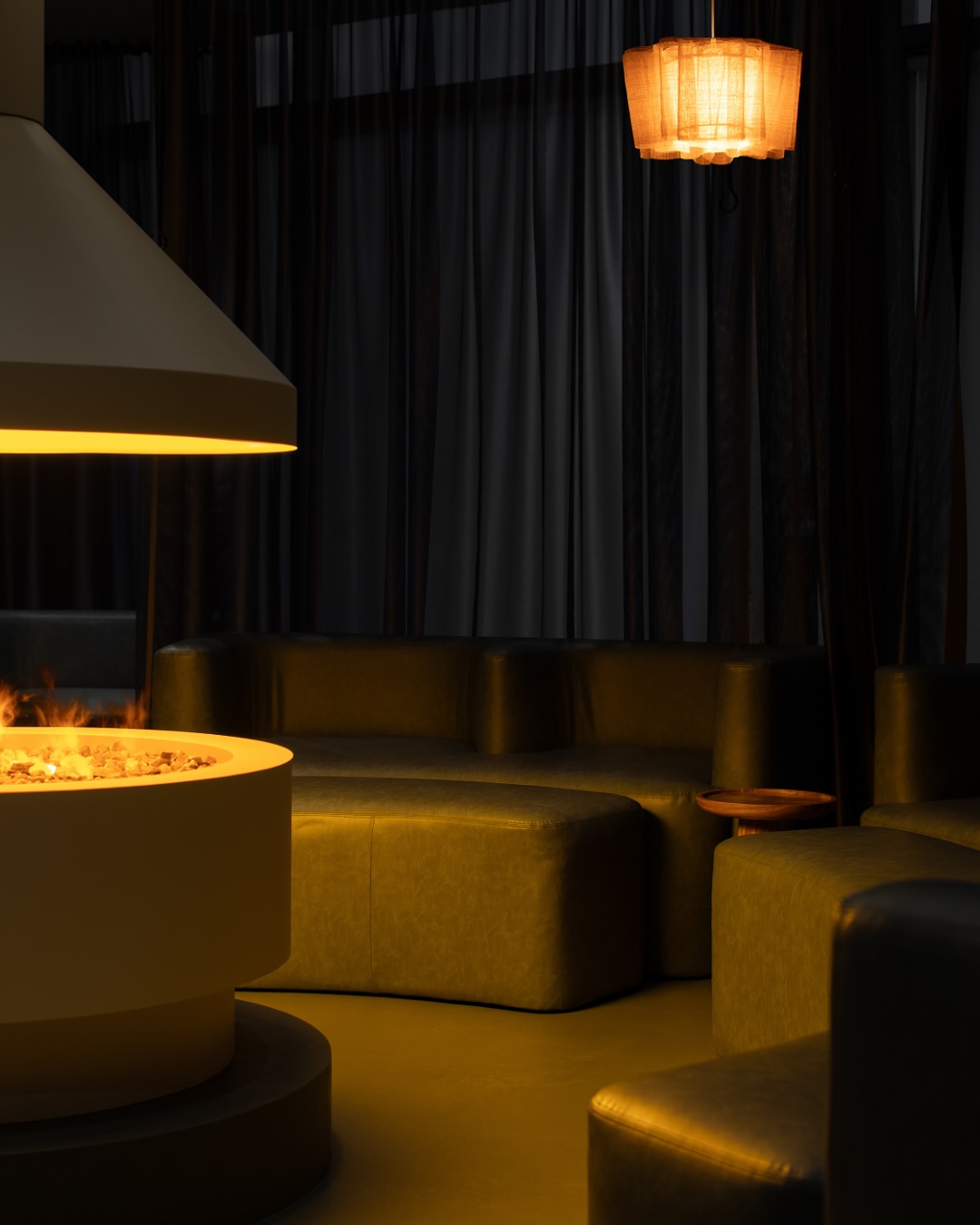 Trove | Dimly lit room with round white fireplace in the center with low, soft green leather seating | Homes Almanac