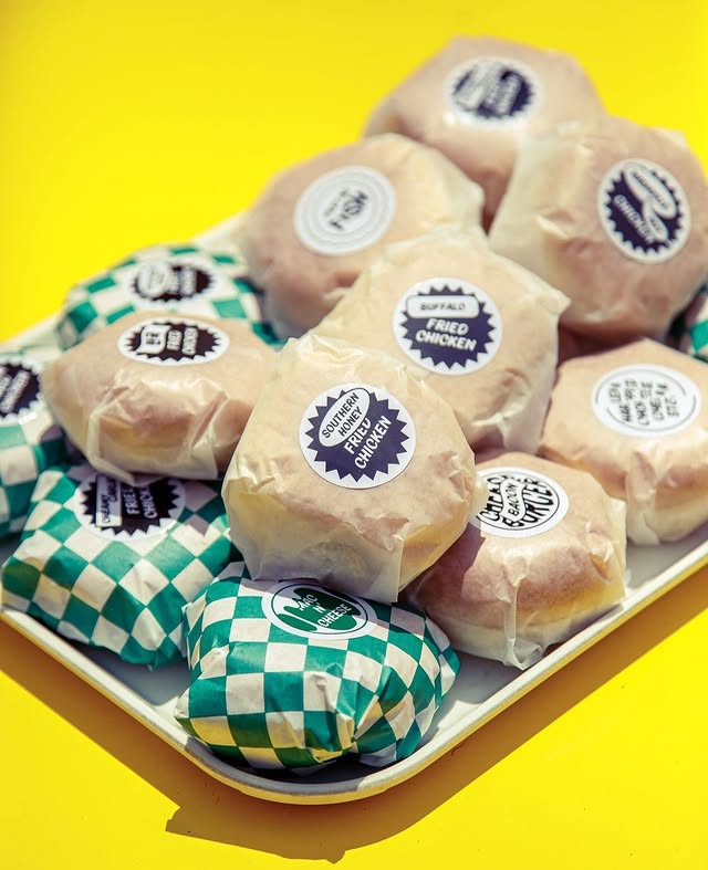 Pennies Toronto | A pile of slider burgers wrapped in white and green checkered wrapper paper on a yellow table | Homes Almanac