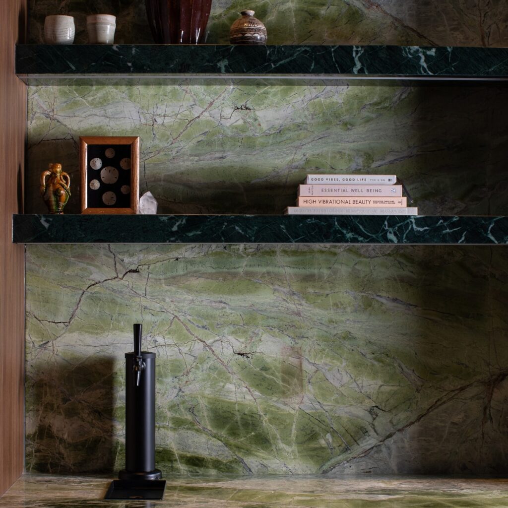 trove wellbeing | green marble wall and dark green marble shelving with books and trinkets hovering over a black hot water dispenser on the counter | Homes Almanac