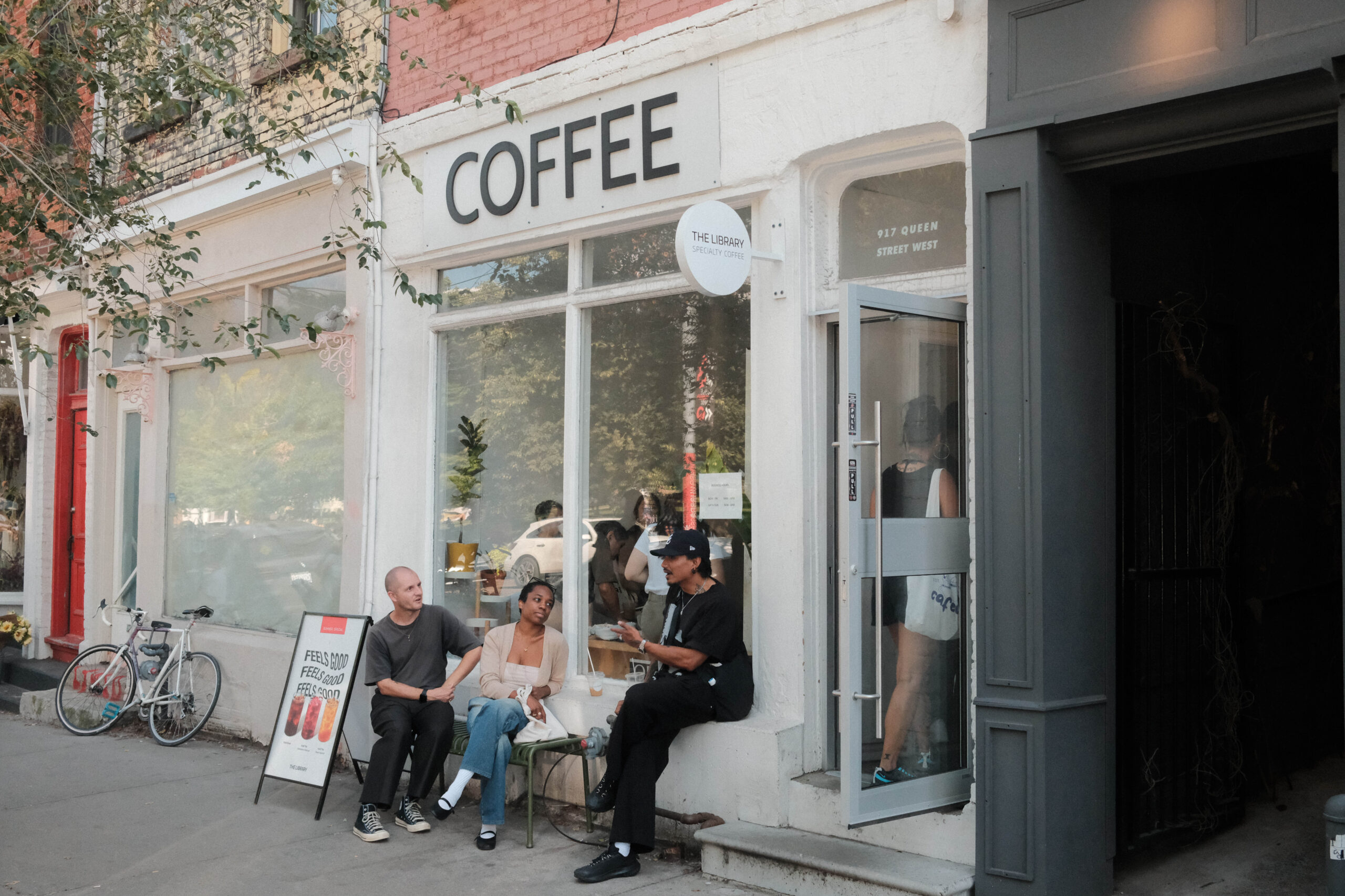 The Library Specialty Coffee on Queen | People sitting outside a white facade coffee shop | Homes Almanac
