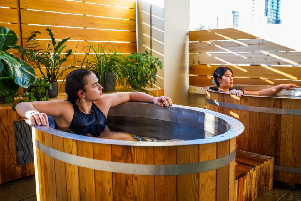 Orijin Yoga studio in Collingwood | Sheltered outdoor space with two people in wooden cold plunge pools relaxing | Homes Almanac