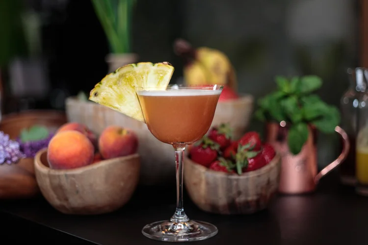 fermentation cocktails toronto | an orange cocktail in a glass with peaches and strawberries in the background | Homes Almanac