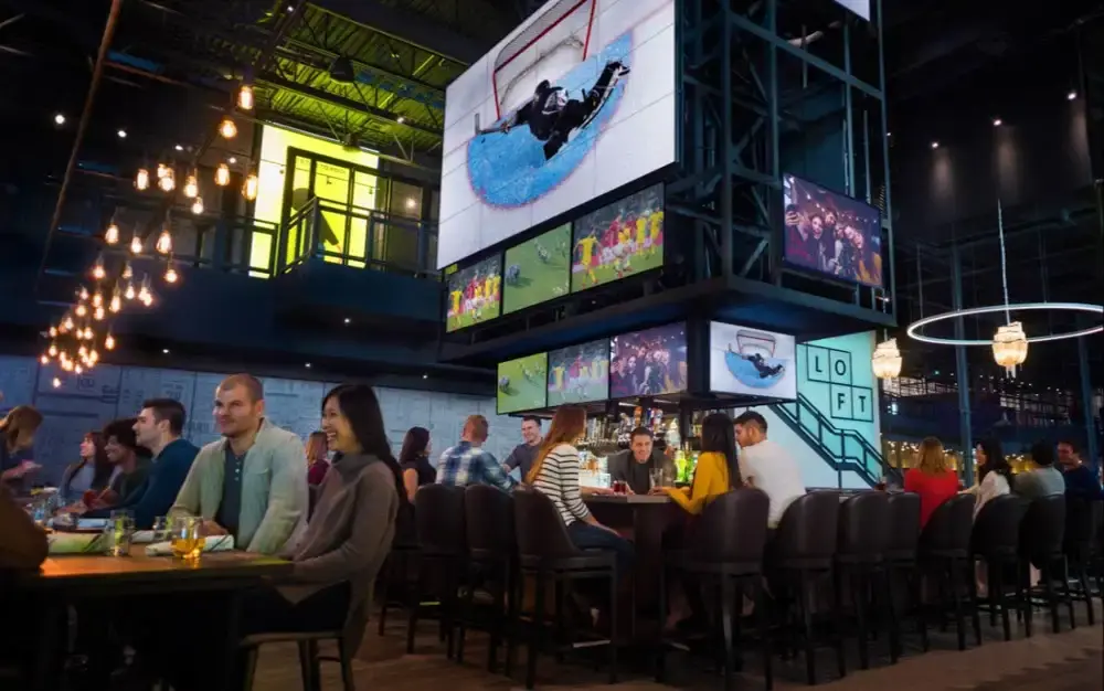 The Rec Room Roundhouse | Sports bar with large screens and people sitting at tables | Homes Almanac