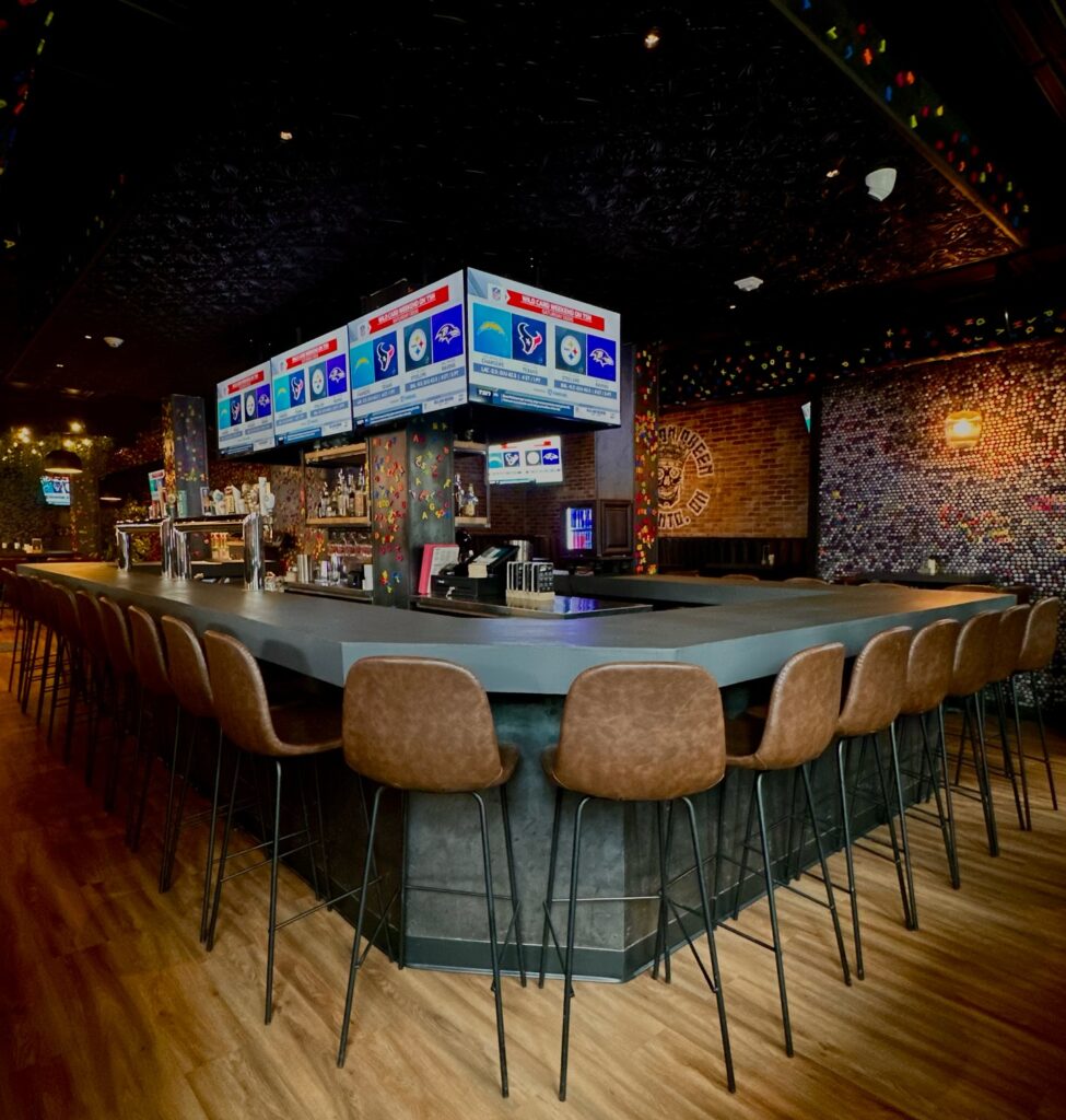 Score on Queen | Dimly lit sports bar with leather high top chairs at the bar and tv screens | Homes Almanac