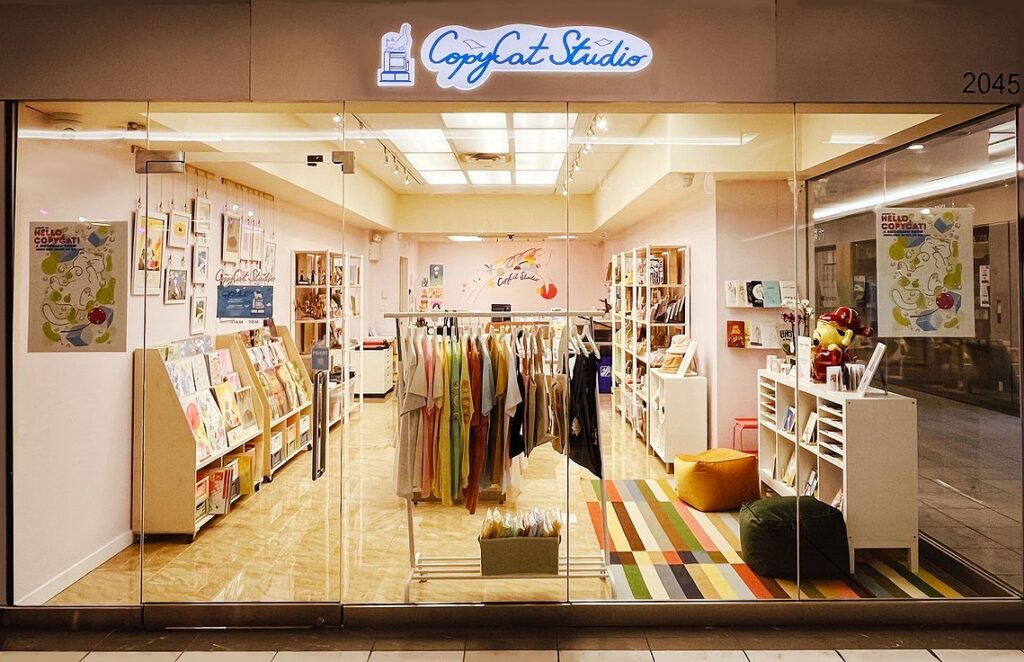 Copycat Studio Risograph Printing Richmond | Brightly lit storefront exterior of an artist retail shop with racks of shirts at the front and shelves of prints and merchandise on both sides of the store | Homes Almanac