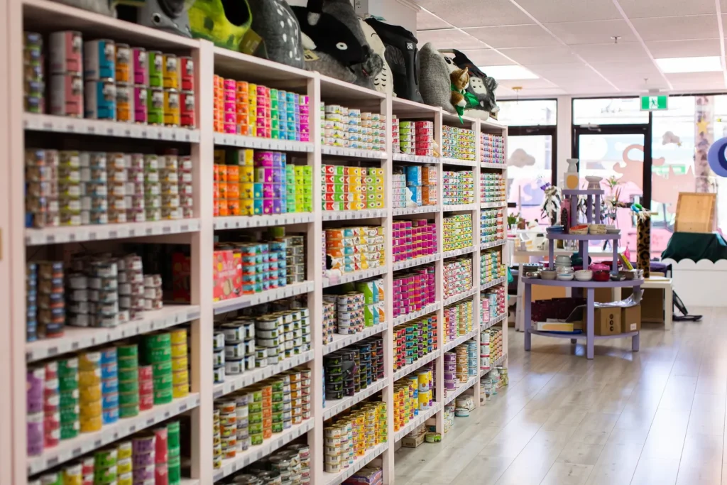 Happy Cat Feline Essentials Supply Store Vancouver | Shop interior lined with shelving filled with various brands of canned cat food, and off to the side a tiered table with cat food bowls | Homes Almanac 