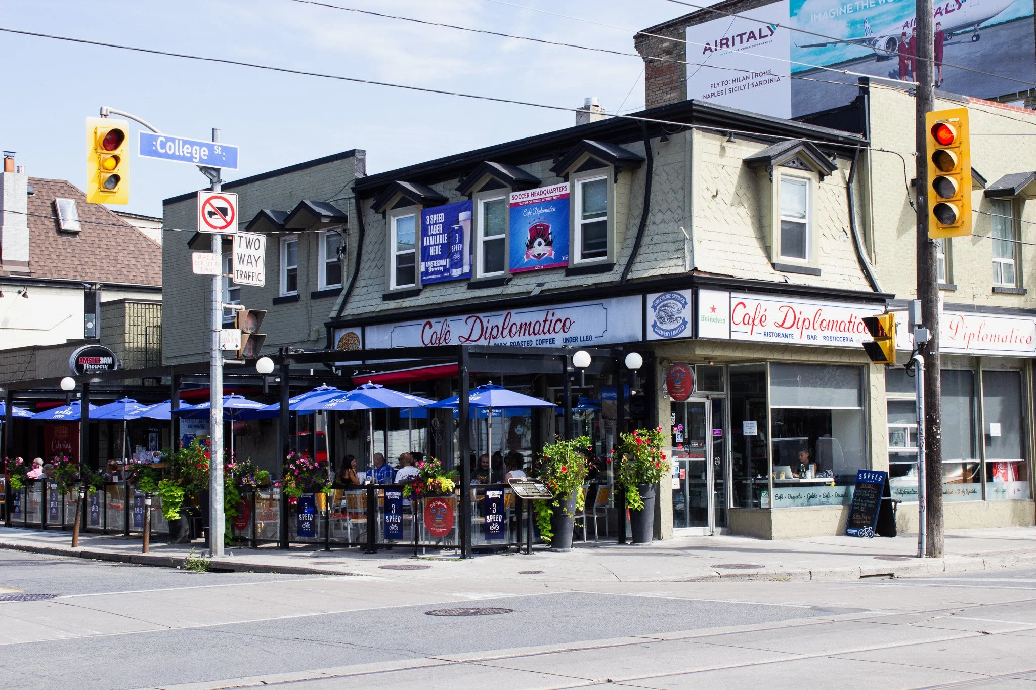 Cafe Diplomatico | External shot of coffee shop on the corner of the street with blue umbrellas outside on a sunny day | Homes Almanac