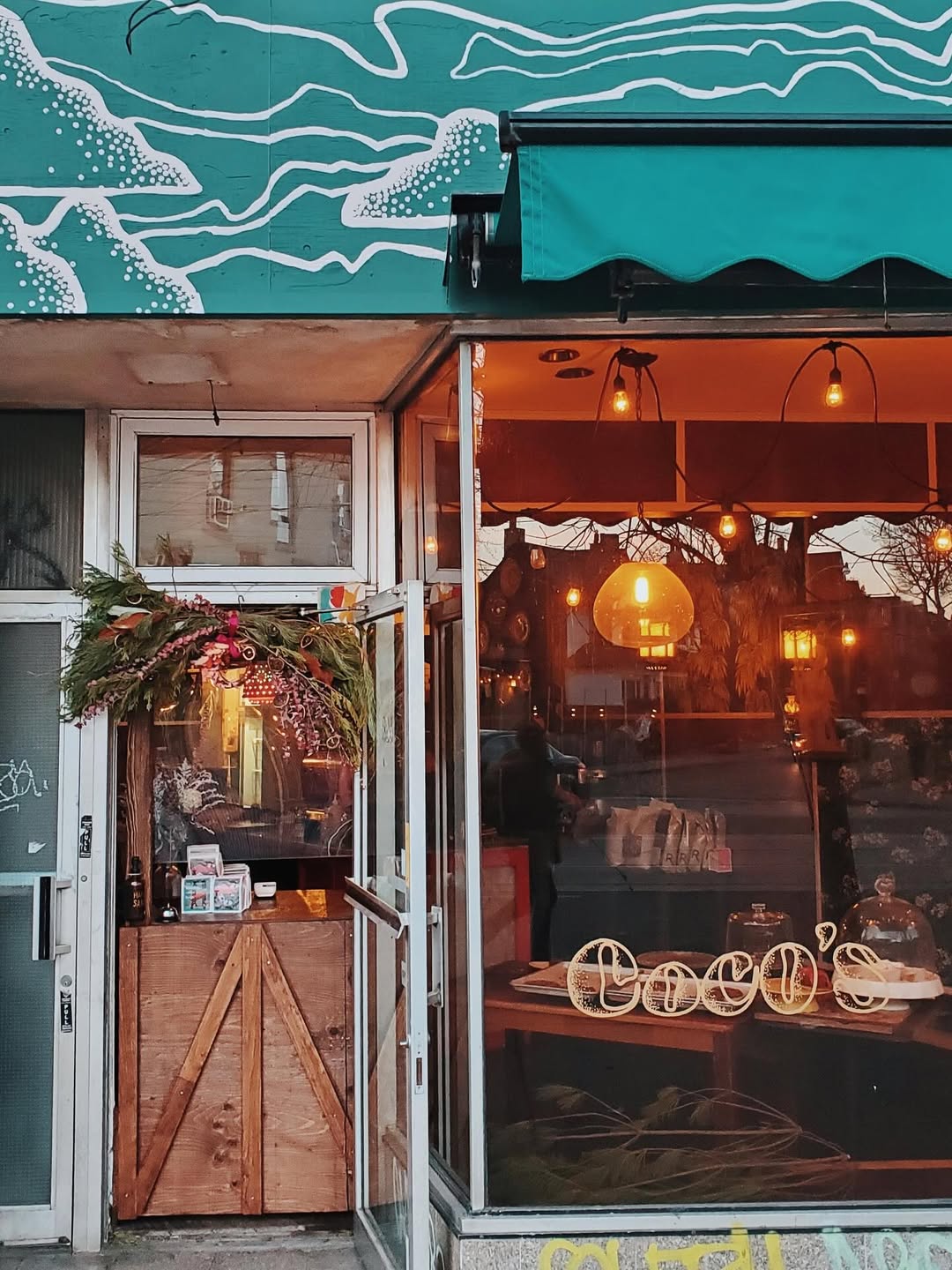 Coco's Neighbourhood Coffee Shop | Quaint exterior of a coffee shop with green awning and arm lighting through the windows | Homes Almanac