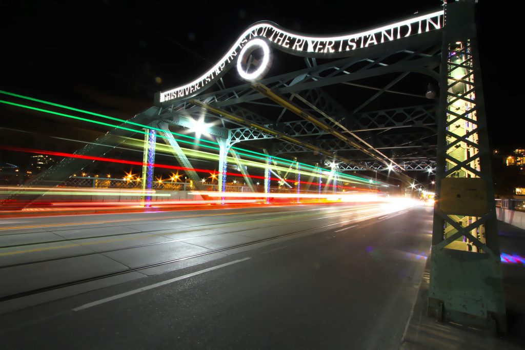 Night shot of the Queen Street Viaduct Bridge that reads “The River I step in is not the River I stand in.” | Queen street toronto street art | Homes Almanac