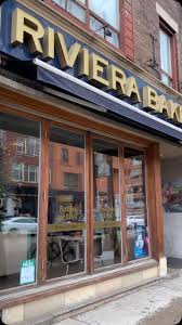 Riviera Bakery | Exterior shot of bakery with floor to ceiling glass windows and yellow logo sign | Homes Almanac