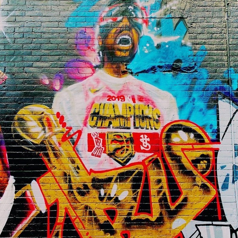 Bright mural of a man holding a basketball trophy dated 2019 | Queen Street Toronto Street Art | Homes Almanac