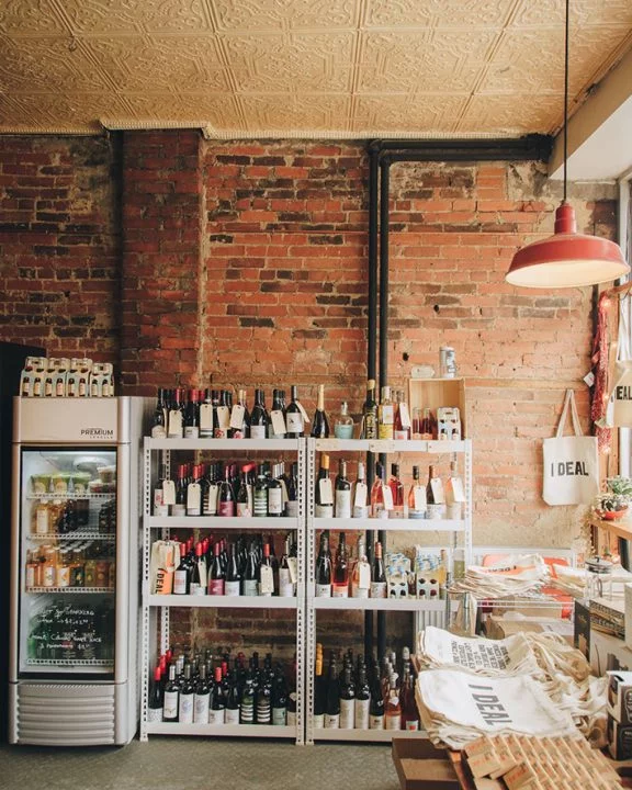I Deal Coffee & Wine on Sorauren | Red brick wall with shelves of wine bottles, a red lamp hanging from the ceiling and light on the right from a window | Homes Almanac