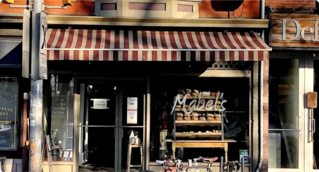 Mable's Bakery in Roncesvalles | Morning light hits the bakery exterior with a red and white striped awning and shelves of bread through the window | Homes Almanac