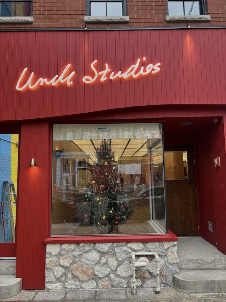 Uncle Studios | Red exterior with Uncle Studios logo written in italics and floor to ceiling windows with a christmas tree | Homes Almanac